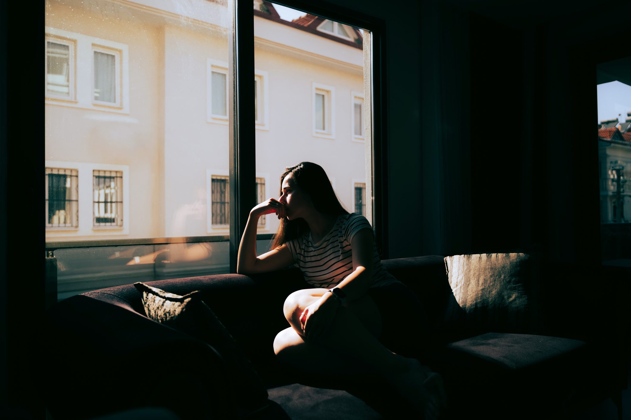 Woman is sitting on the sofa near the window at home.